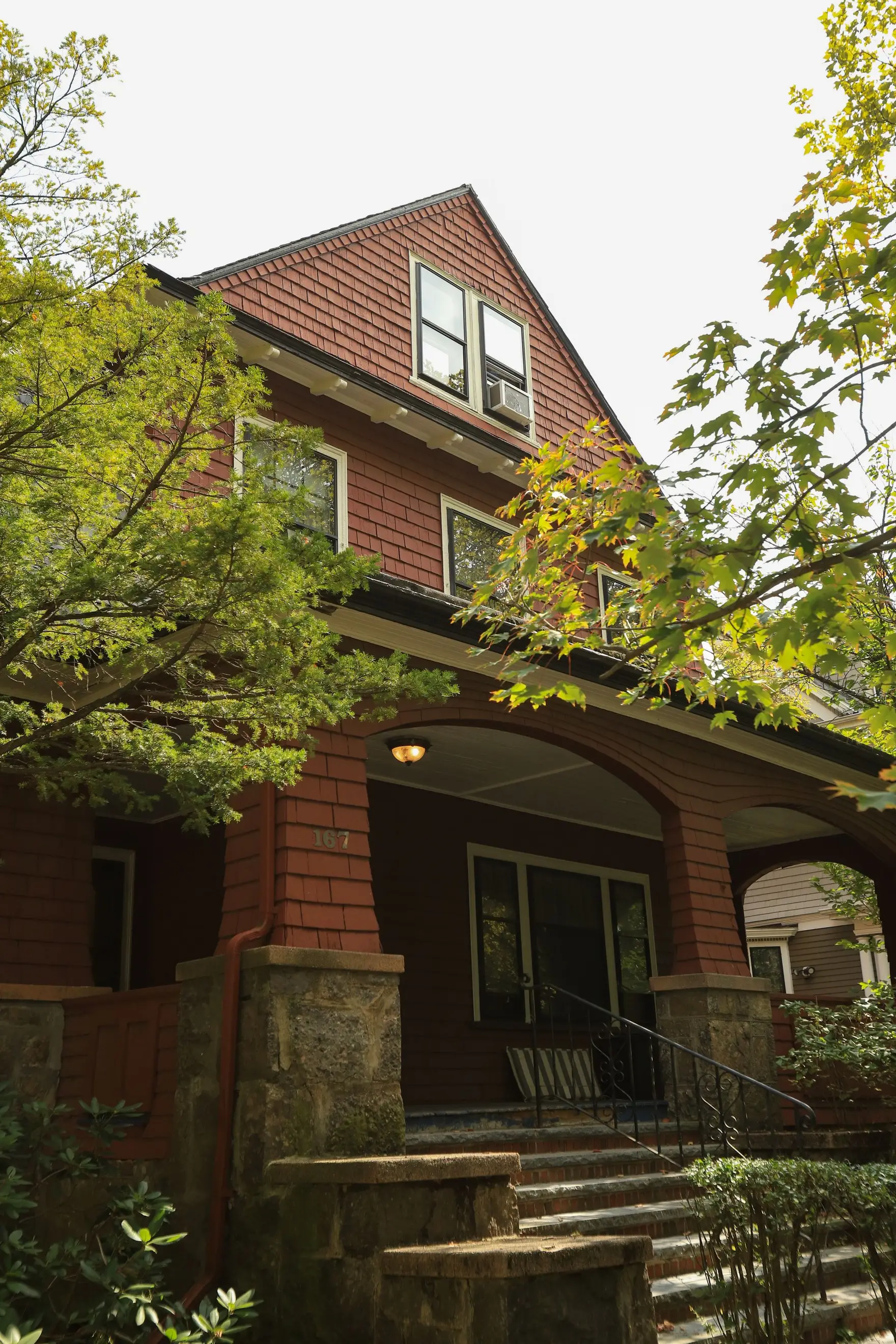 Shingled Craftsman-era house with an arched front porch, framed by mature trees