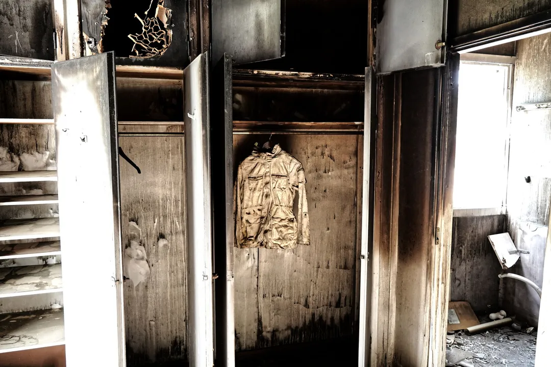 Fire-gutted room with soot-blackened cabinets and a scorched jacket