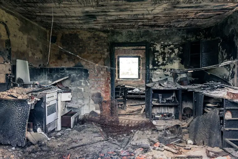 Burned-out kitchen with charred cabinets, scorched walls, and debris